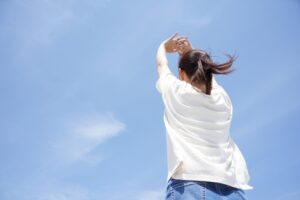 小さな幸せを見つけたかのように、青空にむかってのびをしている女性の写真